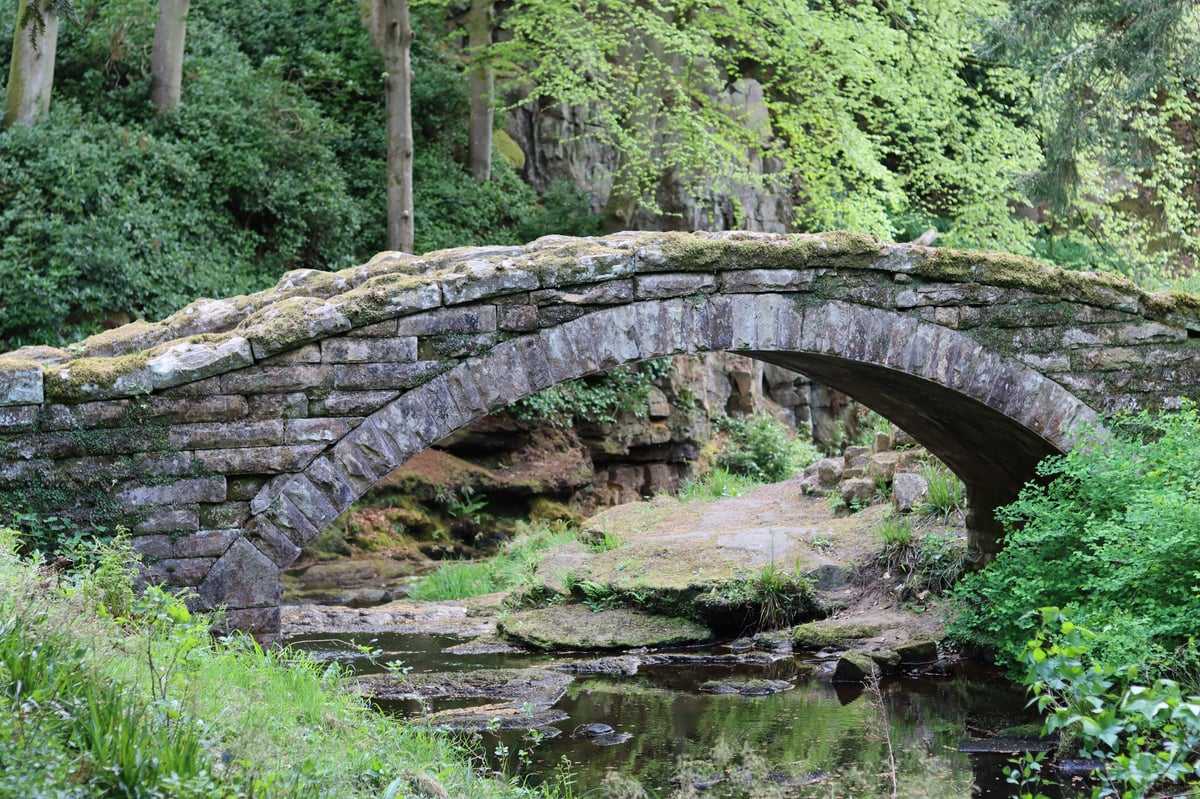 A historic stone bridge arching over a woodland river