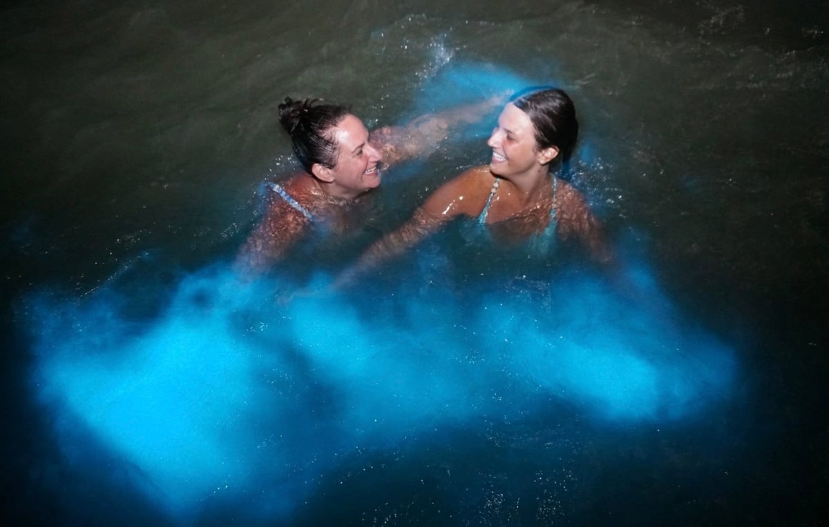 Two people immersed in glowing blue water, surrounded by luminescent blue light effects and mist