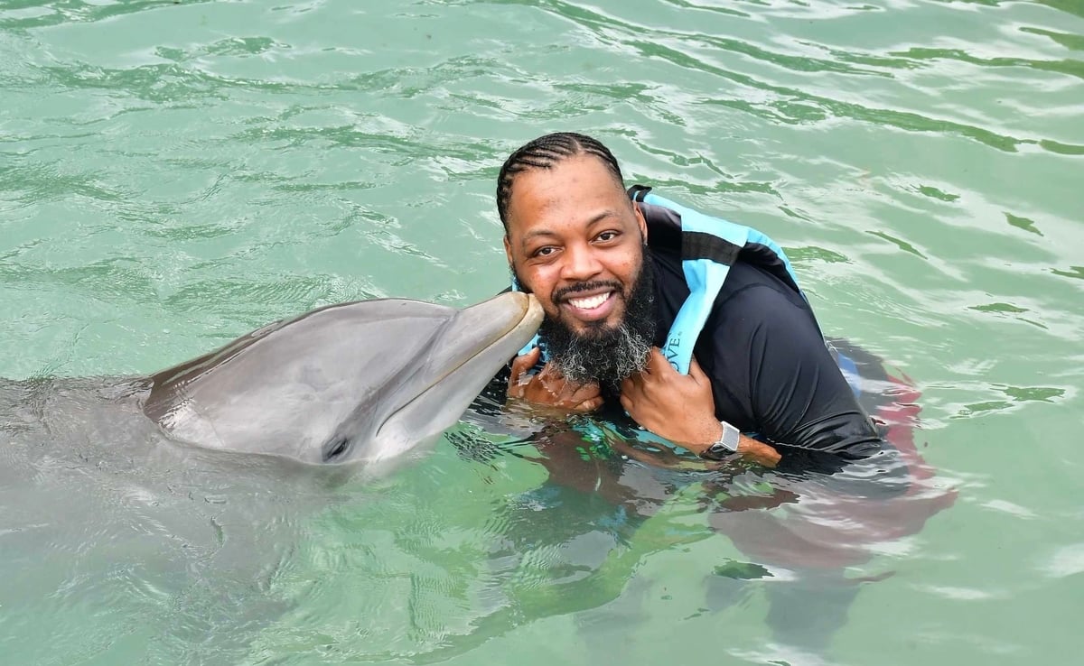 Man smiling while swimming with a dolphin in clear turquoise water