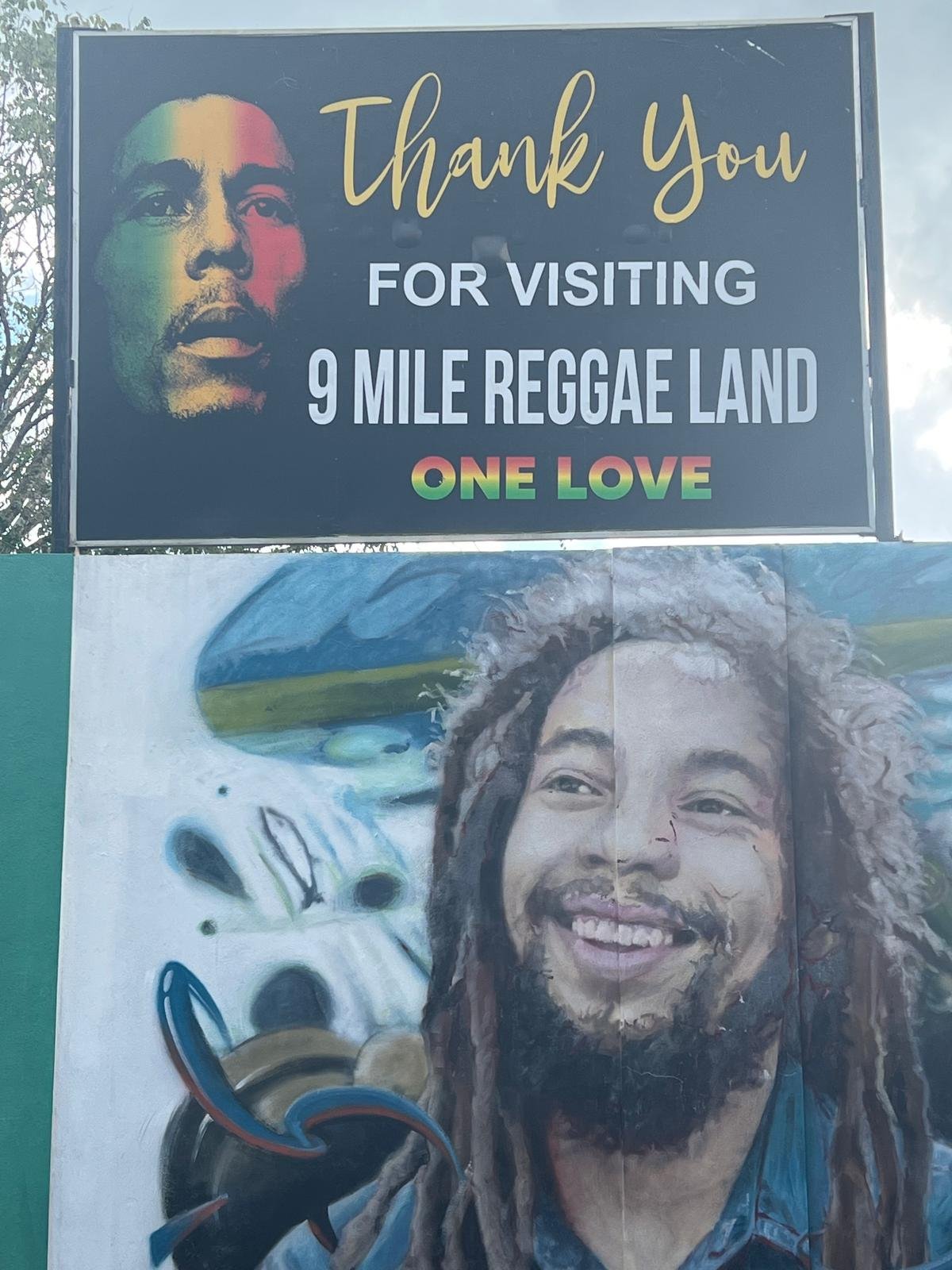 Two roadside signs in 9 Mile Reggae Land featuring reggae artist portraits and One Love messaging
