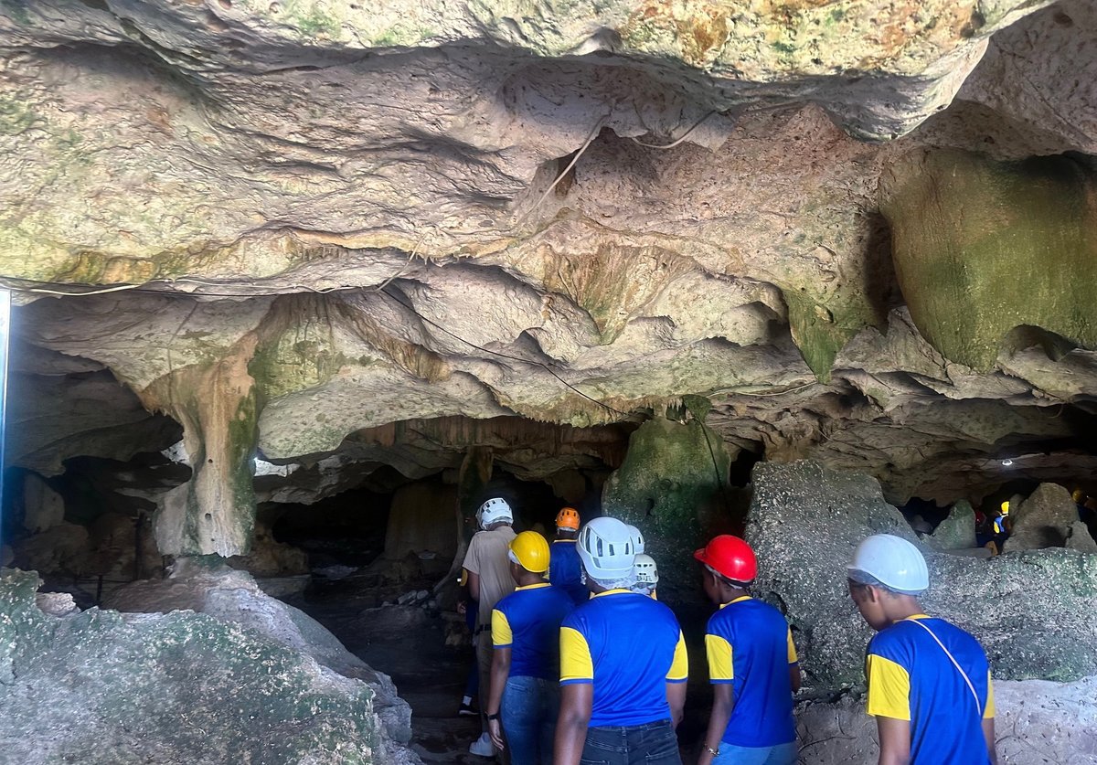 Group of four people wearing hard hats and blue safety vests entering a rocky cave entrance at the Green Grotto Caves in Discovery Bay, St. Ann